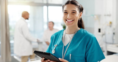 Young nurse wearing scrubs, holding an iPad and smiling