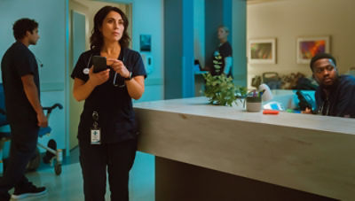 Nurse standing at reception desk looking into middle distance while holding and pointing to mobile phone 