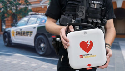 police officer standing in front of squad car holding LIFEPAK CR2 defibrillator