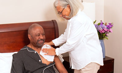 Nurse applying a Sage Comfort Bath cloth to a patient on their bed.