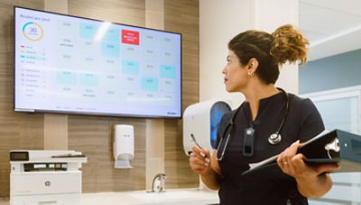 nurse looking at wearing Sync Badge, looking at large monitor on wall