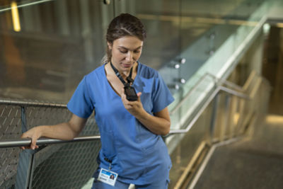 A nurse standing on stairs using a Vocera SmartBadge to communicate hands-free 