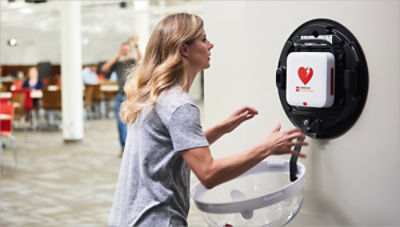 Woman retrieving an AED from a wall cabinet in an office 