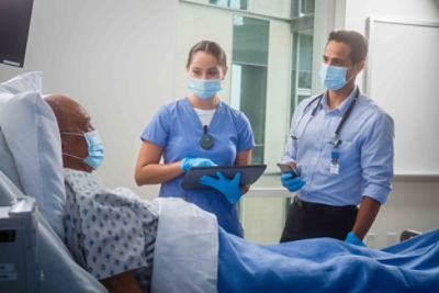 Masked healthcare workers speak with a patient while wearing Vocera Minibadges