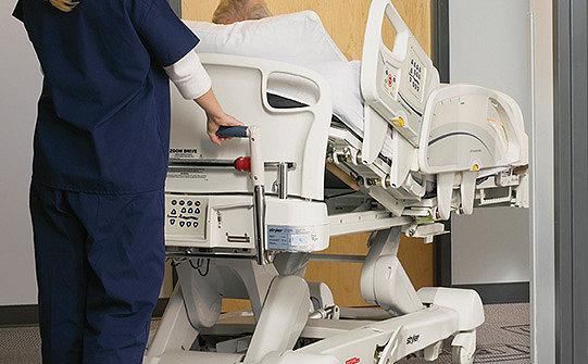 Caregiver using the Zoom Motorized Drive System on Stryker's InTouch Critical Care Bed
