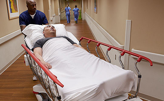 Membru al personalului medical împingând un pacient așezat pe targa Prime X de la Stryker