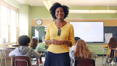 teacher wearing Sync Badge is standing in classroom with students behind her