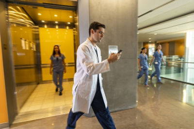 doctor walking briskly while looking down at phone.