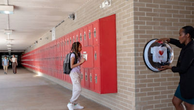 Teacher accessing Lifepak CR2 AED wall unit next to student opening locker