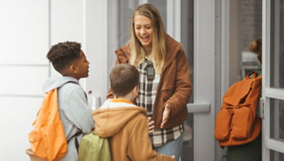 Teacher wearing Vocera Smartbadge greeting students at front door of school