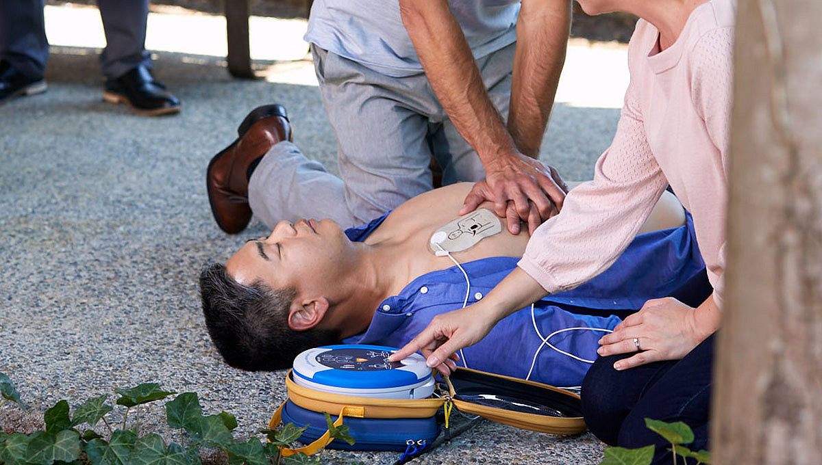 Two bystanders perform CPR on a sudden cardiac arrest victim, one uses a HeartSine 360P on the victim 