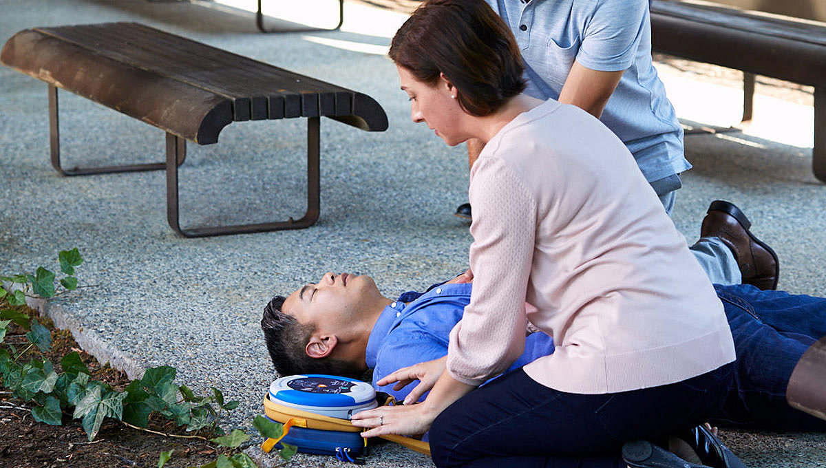 Homme couché au sol à côté d'une femme équipée d'un dispositif HeartSine
