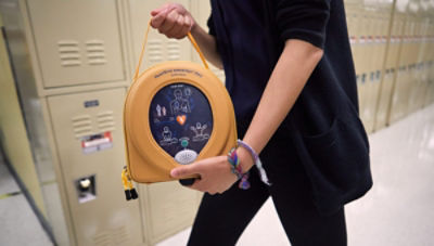 A teacher carries a HeartSine samaritan PAD 450P through a school hallway 