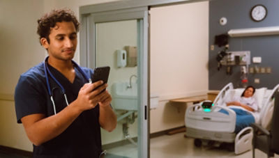 Nurse looking at phone, patient in ProCuity bed in background