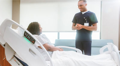 Nurse chatting with patient in a ProCuity bed about steps to prevent infection in the hospital.