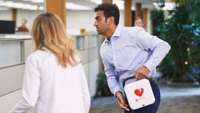 Man carrying LIFEPAK CR2 unit with woman responding to cardiac arrest in office setting