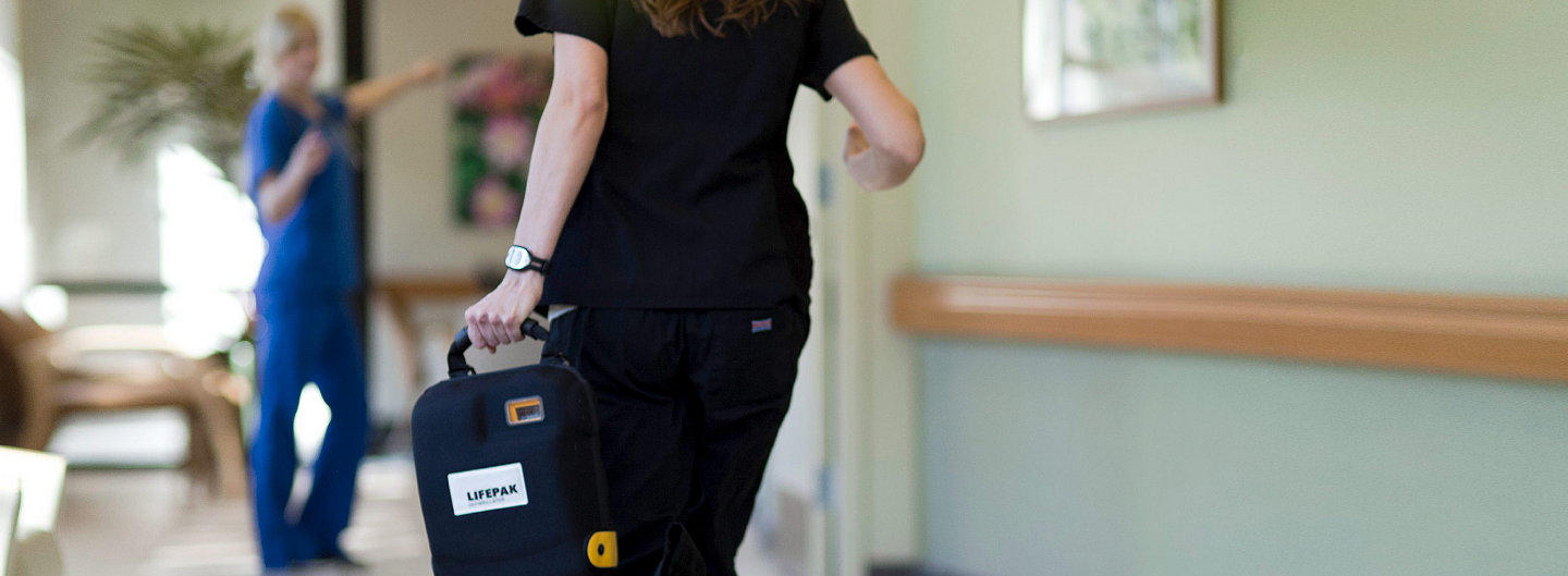 Nurse running down hall holding a LIFEPAK 1000 defibrillator