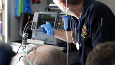 Un paramedic indică defibrilatorul-monitor LIFEPAK 15 în spatele unei ambulanțe