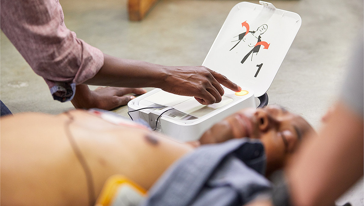 Mężczyzna leżący na ziemi z defibrylatorem AED LIFEPAK CR2 podłączonym do klatki piersiowej i kobieta obsługująca urządzenie