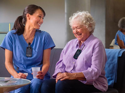 Long-term care nurse sitting on sofa with patient wearing Vocera badges