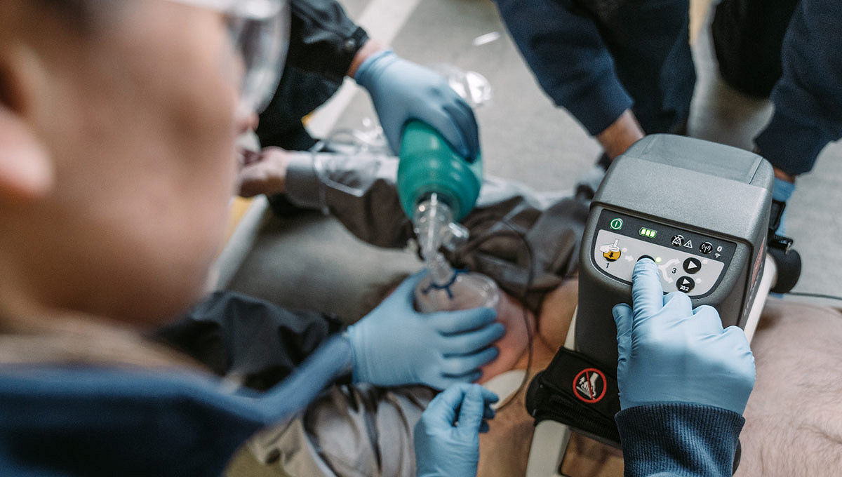 Three EMTs use the LUCAS chest compression machine  on a patient in a public setting 