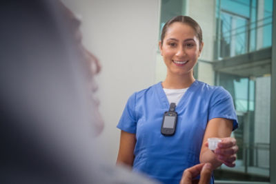 A nurse taking care of a patient while wearing the Vocera Smartbadge on her scrubs