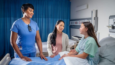 Nurse talking to family member and patient in hospital bed