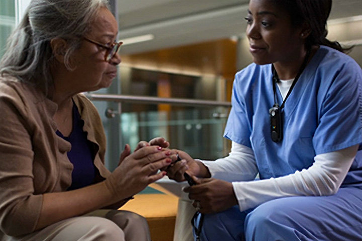 A long-term care nurse wearing a Vocera mini badge visits with a patient