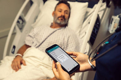 Nursing reading notification on mobile device, patient in hospital bed